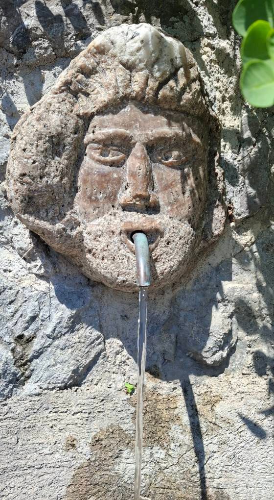 Vecchio fontanile decorativo in pietra con testa umana scolpita e tubatura in ferro che eroga acqua tra le rovine della della Torre dello Ziro 
