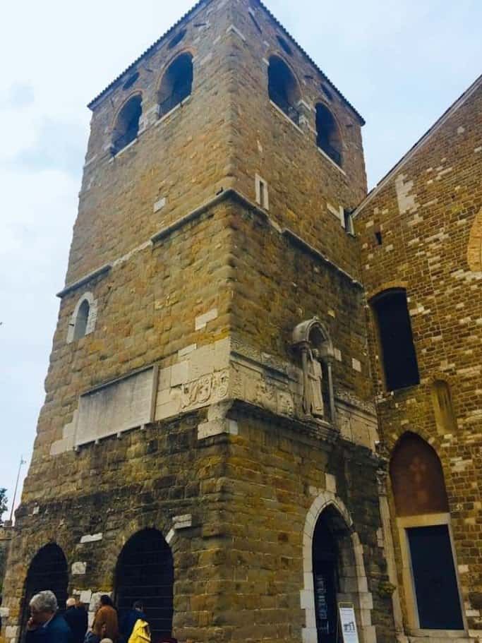 Torri di un antico edificio storico in pietra con nicchie e finestre ad arco, atmosfera medievale, turisti che visitano la struttura.