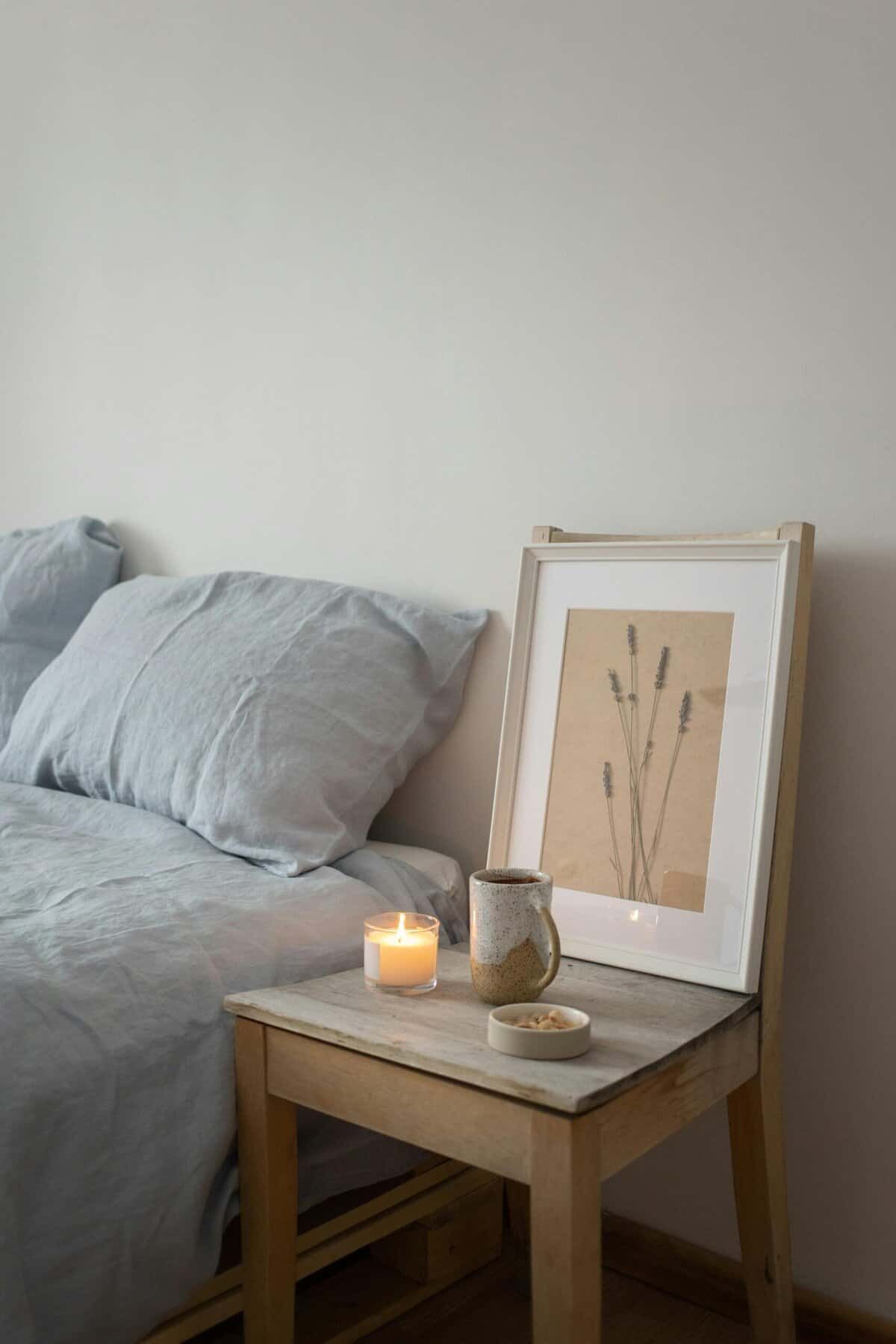 10 vantaggi delle candele aromatiche per migliorare la salute. Luminosità morbida con candela accesa, decorazioni minimaliste e quadro con fiori essiccati sul comodino in legno per un'atmosfera rilassante e accogliente.