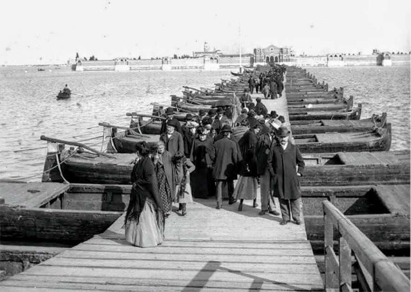Tradizione del Ponte votivo San Michele Venezia 4 Immagine storica del ponte votivo fatto di barche con cittadini in abiti d'epoca, rappresenta la vita quotidiana nel passato marittimo.