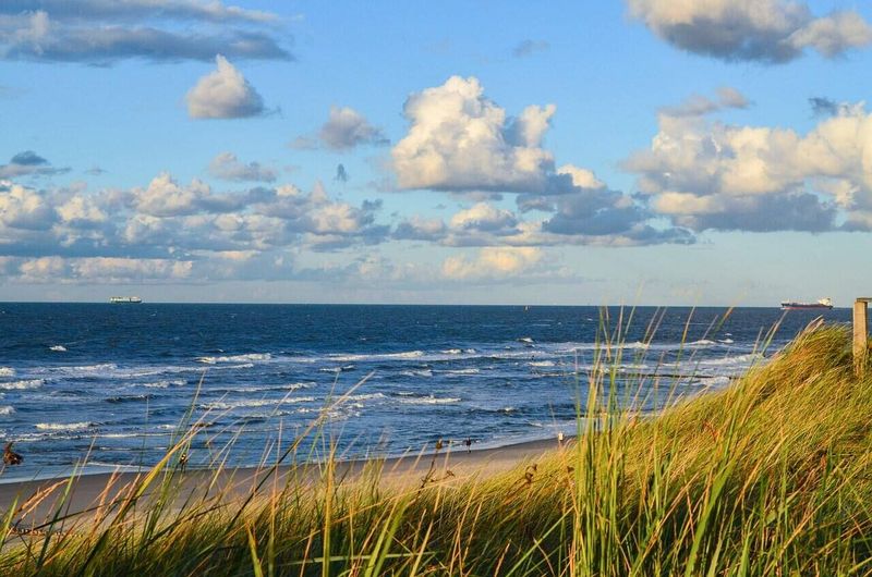 Prenota ora le tue vacanze per trovare le occasioni migliori 2 Prenota ora le tue vacanze per trovare le occasioni migliori. Tramonto sulla spiaggia con onde e cielo nuvoloso, vista panoramica del mare e delle dune di sabbia con erba alta, atmosfera tranquilla e paesaggio naturale.