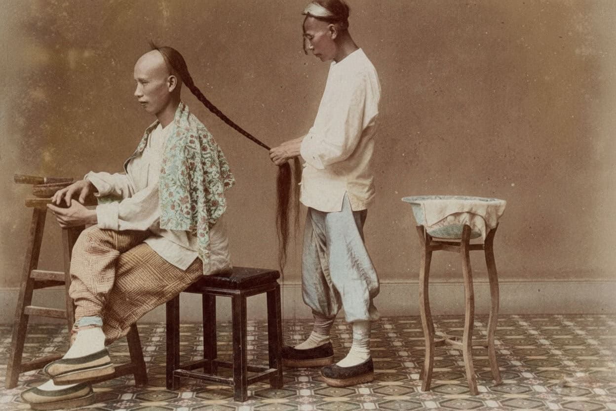 due uomini in abiti tradizionali Qing, uno seduto mentre l'altro intreccia una lunga treccia manciù, interno, stile foto antica, pavimento decorato, atmosfera serena