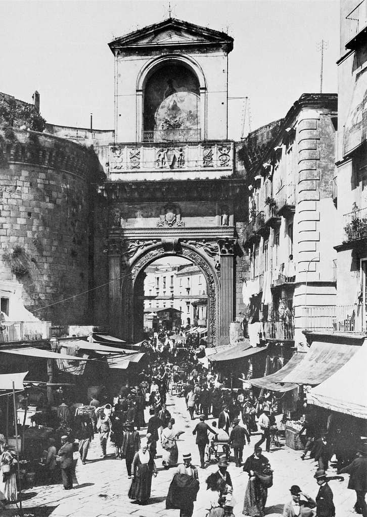 Vicolo storico di Napoli con mercato all'aperto, architetture antiche e strada affollata di cittadini e turisti, atmosfera vibrante e autentica del centro storico.