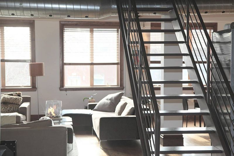 Quando l'architettura incontra l'Emozione 2 Moderno salotto con grandi finestre e pareti bianche, arredato con divani, lampada da terra e una scala in metallo che collega i piani superiori, in stile industrial chic.