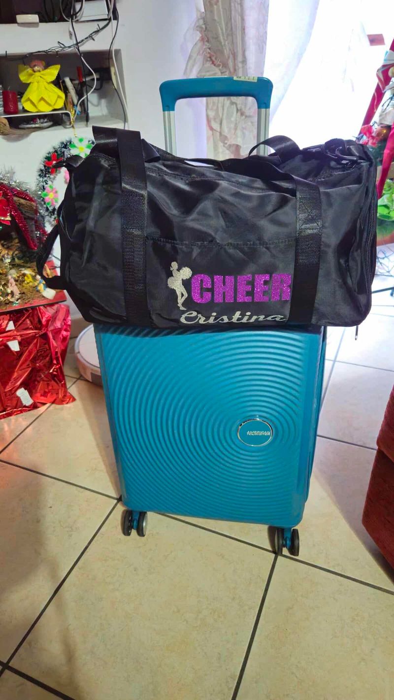 Borsa Donna da Palestra Glitter: Stile e Comfort 5 Valigia blu con ruote e dettagli moderni, pronta per il viaggio, con una borsa di cheerleader sopra.