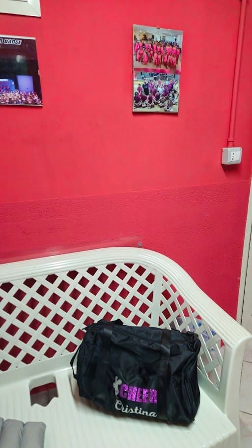 Borsa nera con nome "GFEAR Cristina" su panca di attesa in studio di fisioterapia. Pareti rosse con foto di gruppo di atleti di ginnastica, ambiente motivante e accogliente.