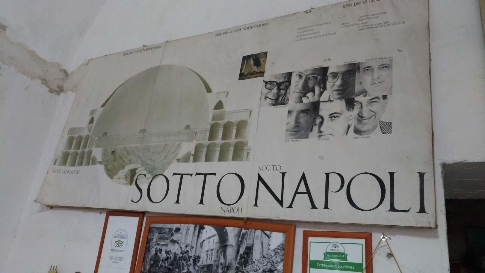 Immagine di un grande cartellone pubblicitario con il testo "SOTTO NAPOLI" e immagini di volti umani e architetture napoletane.