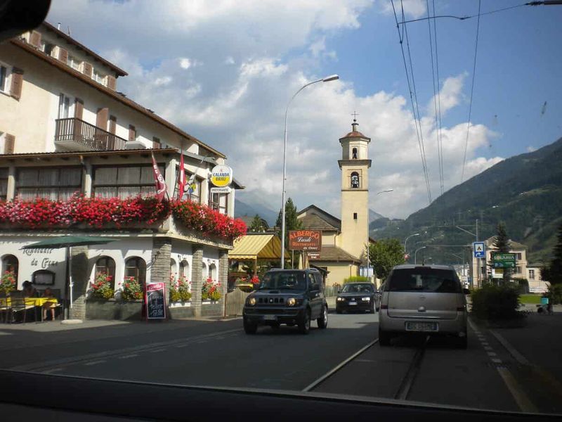 Poschiavo Bernina Express, valle italofona Grigioni Svizzera 2 Vista del centro di Ortisei con chiesa e montagne sullo sfondo, strada trafficata e negozi fioriti, in una giornata soleggiata.