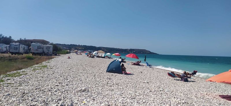 Consigli per le vacanze al mare 5 Spiaggia di ciottoli con ombrelloni colorati, lettini e persone che si rilassano vicino al mare in una giornata soleggiata.
