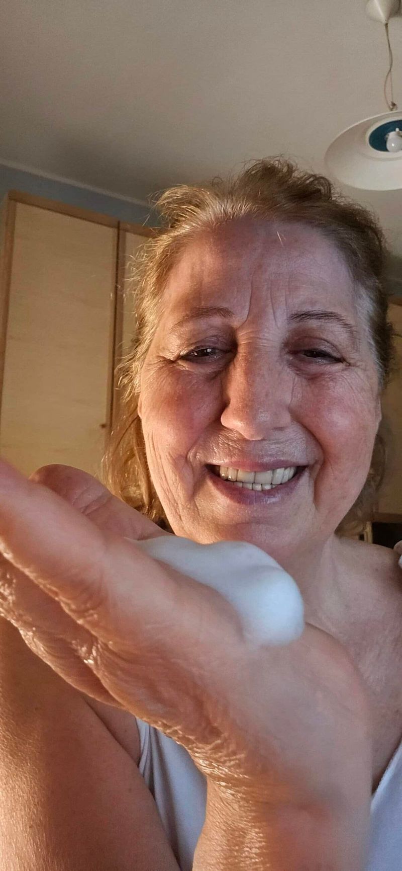 DermaLux Mousse Detergente Viso per pelle matura e spenta 2 Donna sorridente che si lava le mani con sapone in un ambiente domestico, promuovendo igiene e cura personale.