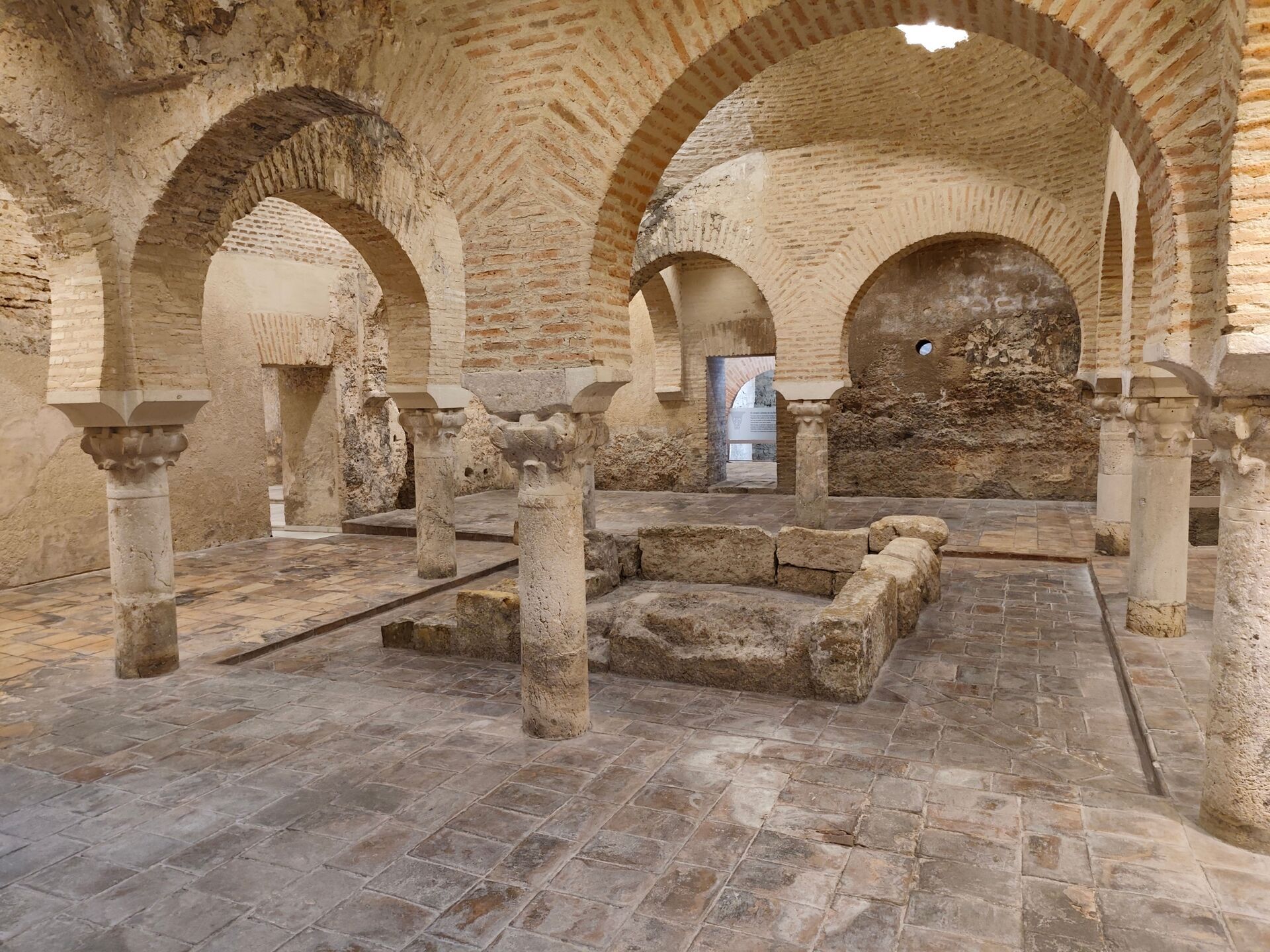 Resti di un edificio storico con archi in mattoni e colonne di pietra, pavimento in pietra e pareti in pietra e mattoni, ambiente interno di un sito archeologico.