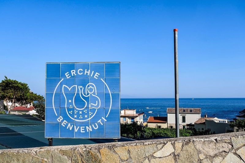 Erchie spiaggia nascosta della Costiera Amalfitana 4 Segnale di benvenuto a Erchie con vista sul mare e case colorate, in una giornata soleggiata e serena.