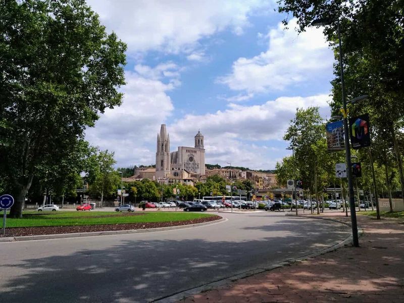 Cosa vedere a Girona in un giorno 2 Sulle orme di Game of Thrones a Girona. Vista della Cattedrale di Girona con il cielo nuvoloso, circondata da alberi e strade trafficate.