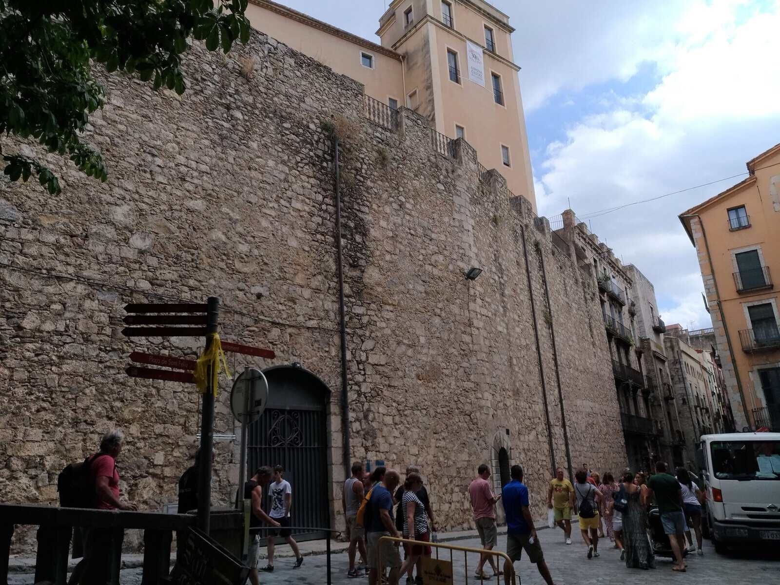 Gruppo di turisti che passeggia vicino alle antiche mura di Napoli, con edifici storici sullo sfondo e un cielo nuvoloso.