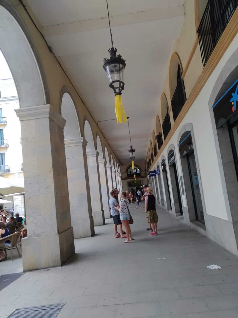 Cosa vedere a Girona in un giorno 7 Passeggiata sotto portici storici con persone che conversano e negozi sul lato destro.