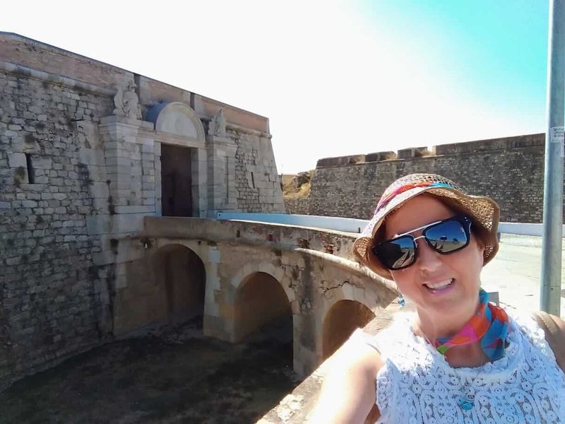 Castello di Sant Ferran a Figueres: la fortezza più grande d'Europa (Orari, Prezzi e Sotterranei) 8 Donna sorridente con cappello e occhiali da sole davanti a una storica fortezza in pietra, in un giorno soleggiato.