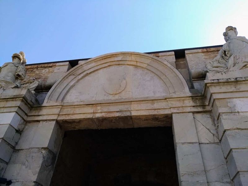 Castello di Sant Ferran a Figueres: la fortezza più grande d'Europa (Orari, Prezzi e Sotterranei) 7 Dettaglio di un arco storico in pietra con statue decorative ai lati, sotto un cielo azzurro.