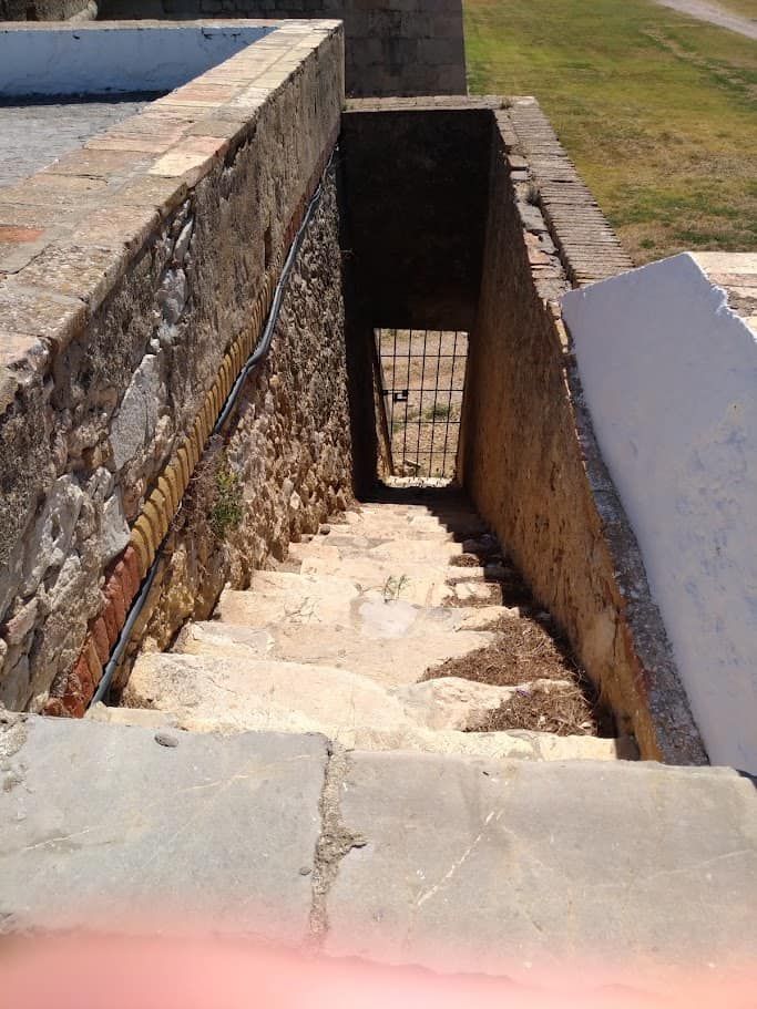 Castello di Sant Ferran a Figueres: la fortezza più grande d'Europa (Orari, Prezzi e Sotterranei) 5 Immagine di una scala antica in pietra che scende in un sotterraneo, con muri in pietra e una porta in metallo alla fine.