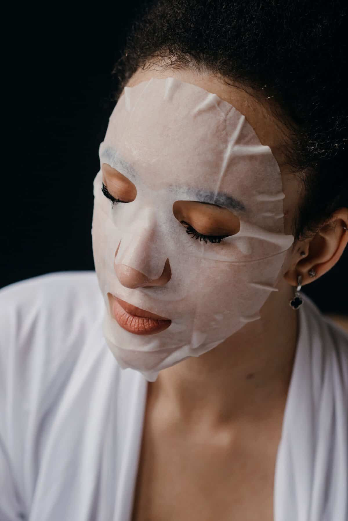 Maschera notte o maschera in tessuto: Close-up di una donna che usa una maschera idratante per la routine di cura della pelle, promuovendo la cura del viso a casa