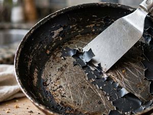 Pentole antiaderenti rovinate: l’errore che può accorciarne la vita 7 Primo piano di padella antiaderente rovinata con rivestimento scrostato e spatola in metallo che graffia il fondo