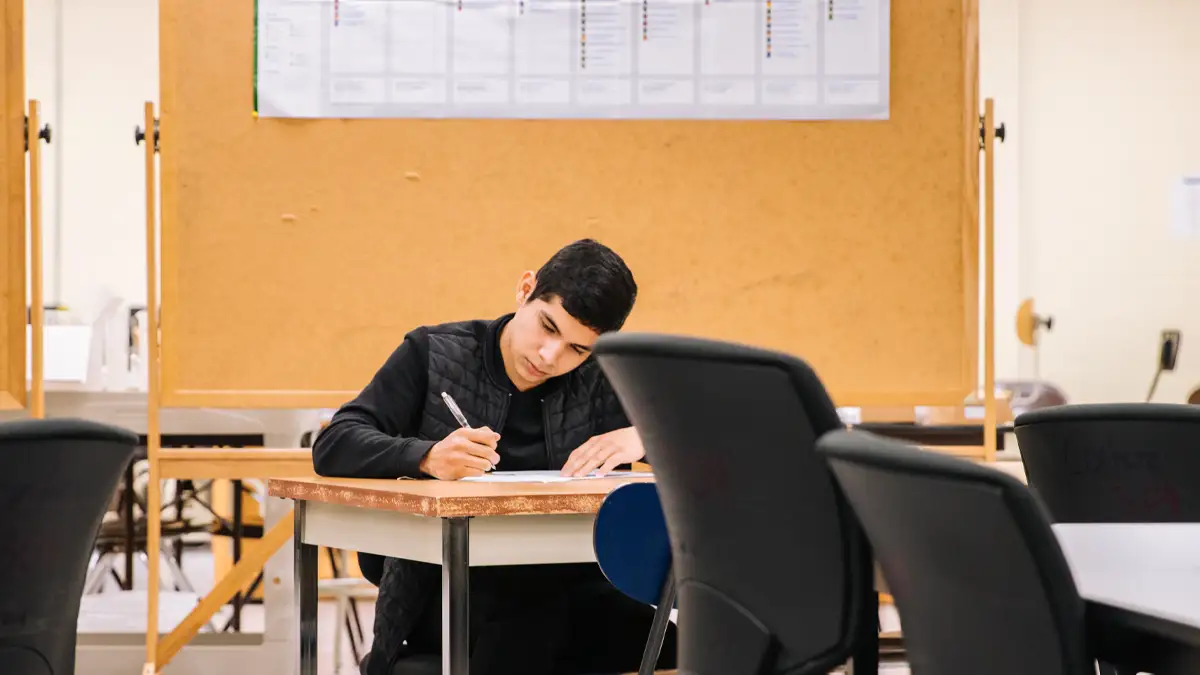Yetişkin bir erkek birey, ahşap bir çalışma masasında elinde kalemle bir form dolduruyor