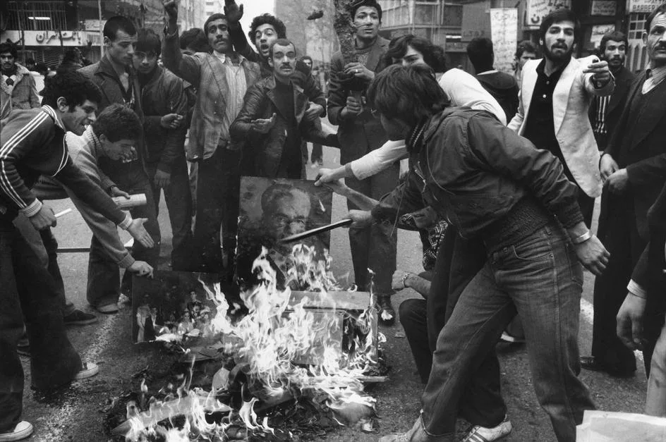 شورشیان به نشانه مخالفت با رژیم درحال سوزاندن عکسی از شاه هستند. تهران، ایران، آذر ۱۳۵۷.