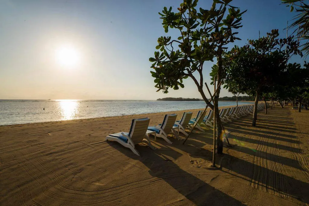 lawn chairs on the beach with sun over the water