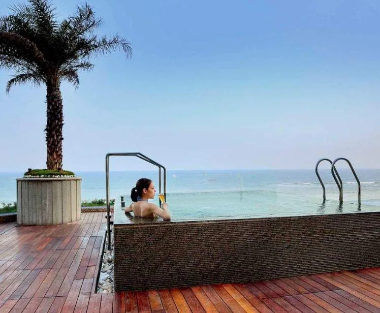 woman in hot tub in front of palm tree and ocean