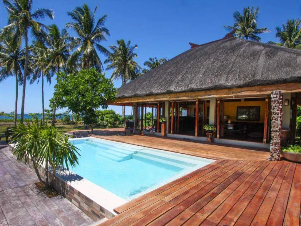 square pool with wood deck surrounded by palm trees