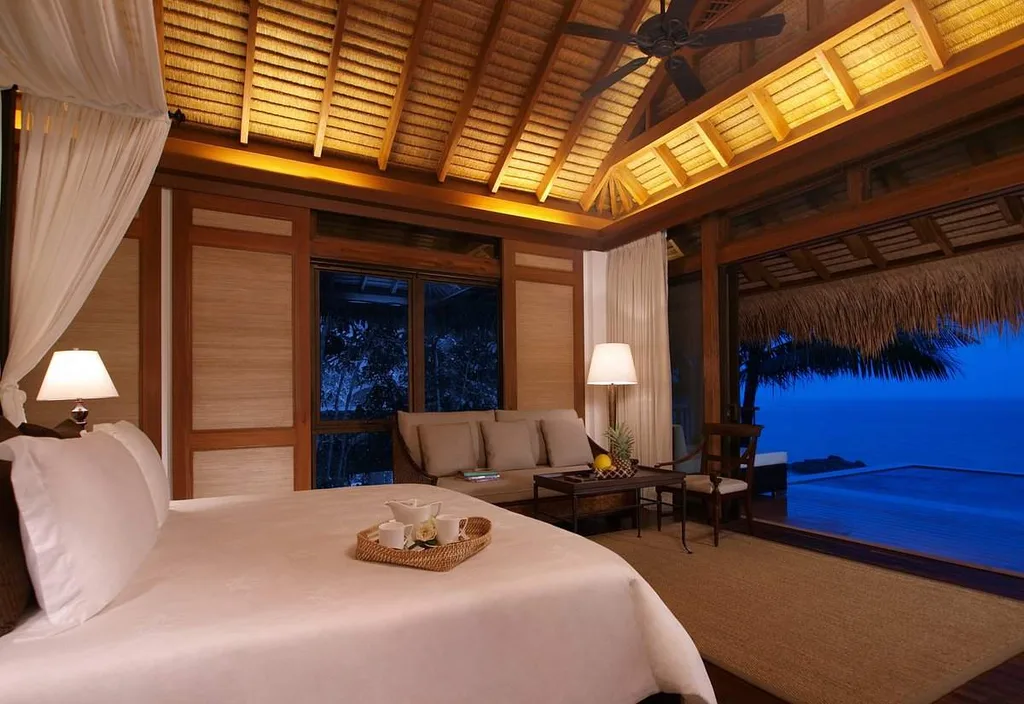 white bed looking out of large window looking at ocean at night