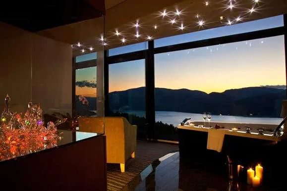 resort room with 3 huge windows looking at mountain behind lake at sunset