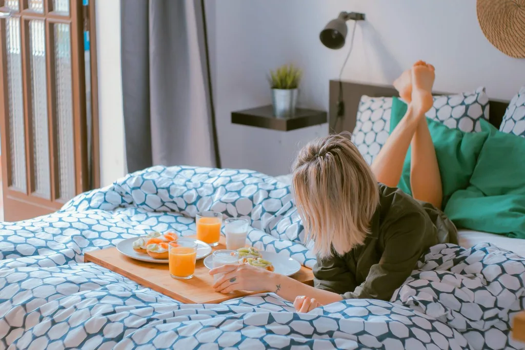 woman lying on resort bed with tray of orange juice and pastries