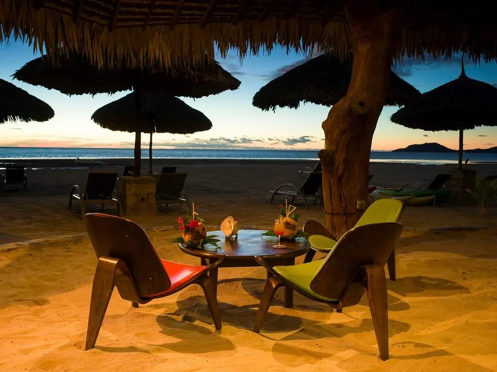 2 chairs with table in front of beach at sunset