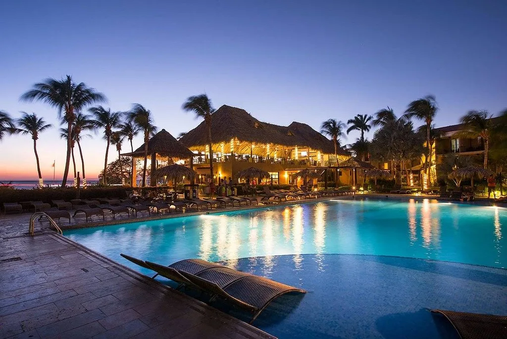 resort pool at night with grass roof building in the back