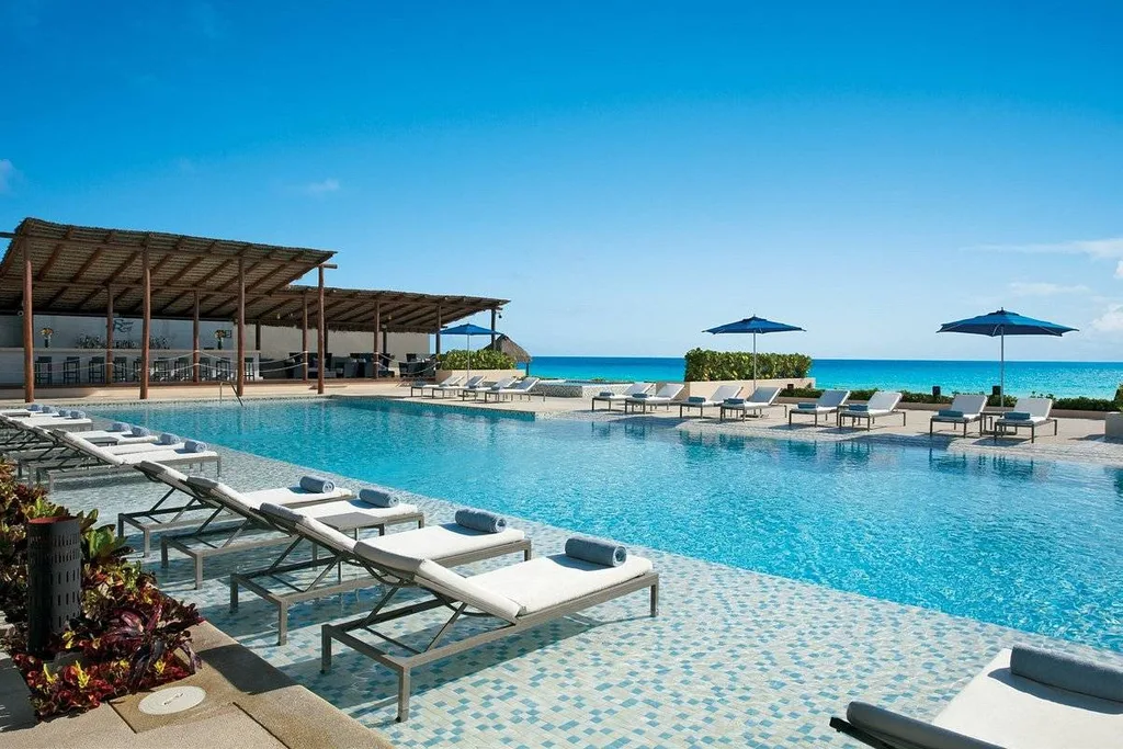 lounge chairs next to rectangular resort pool with ocean in background