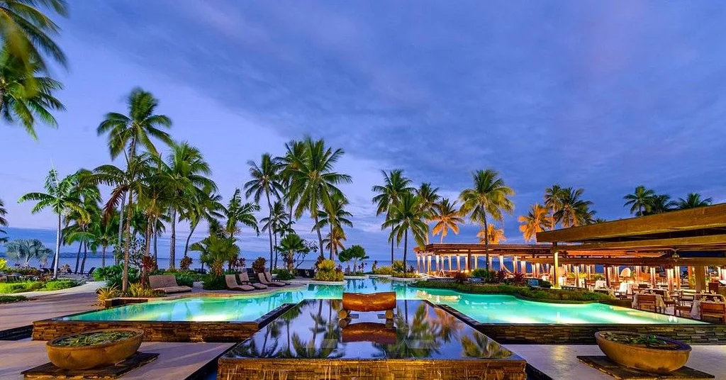 palm trees around lighted resort pool at dusk