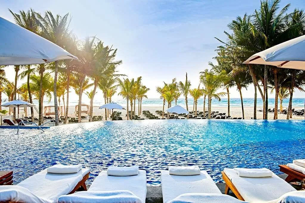 resort pool at the beach with palm trees and white lounge chairs