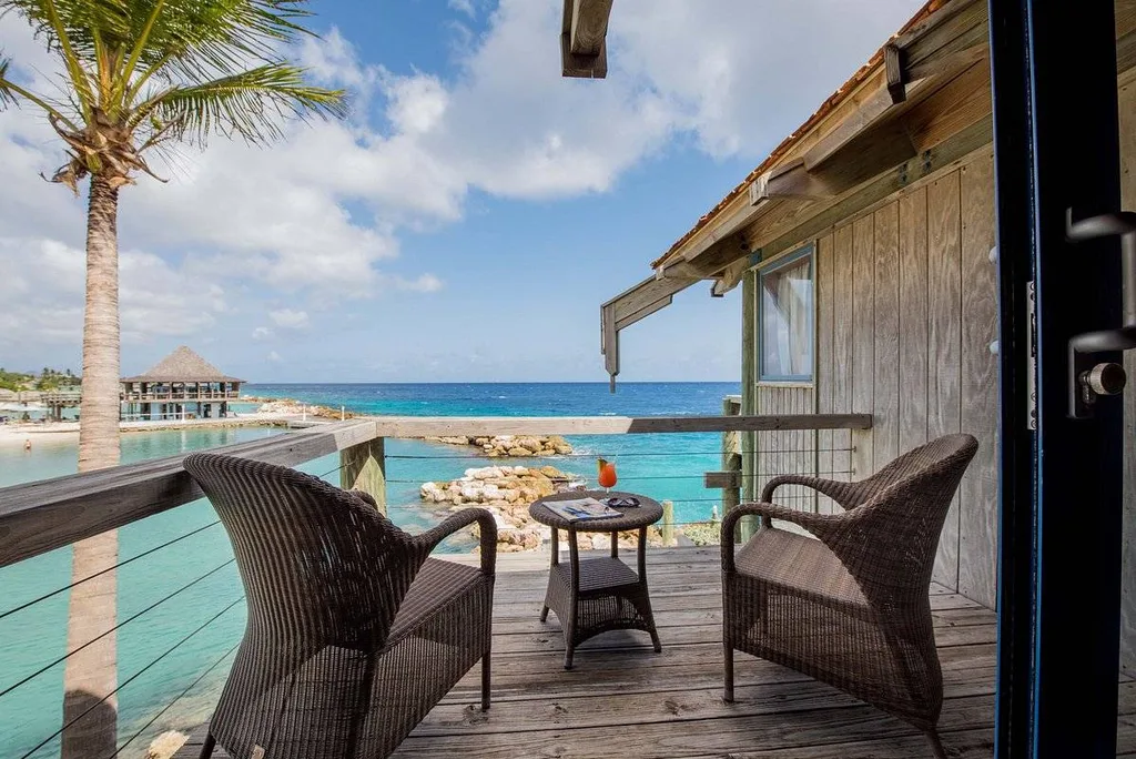 two wicker chairs and table on wooden deck with palm trees