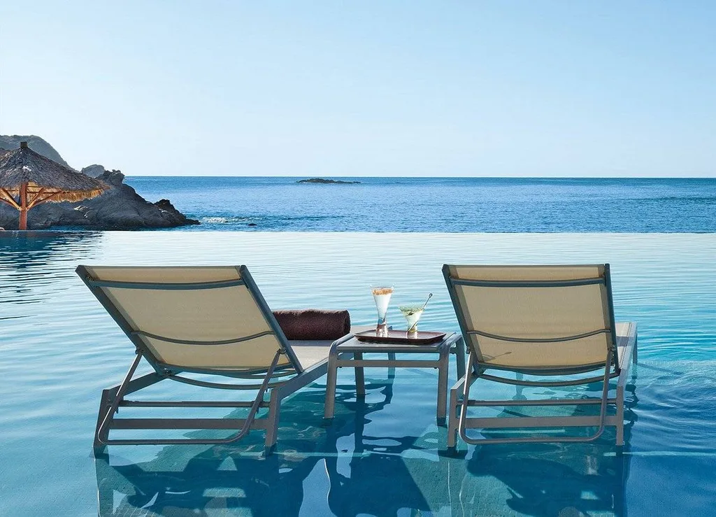 two lounge chairs and table sitting in infinity pool at ocean