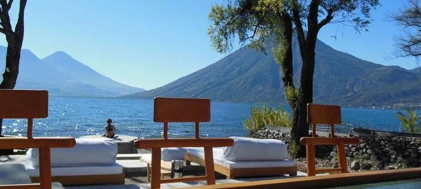 three chairs facing mountains on other side of water