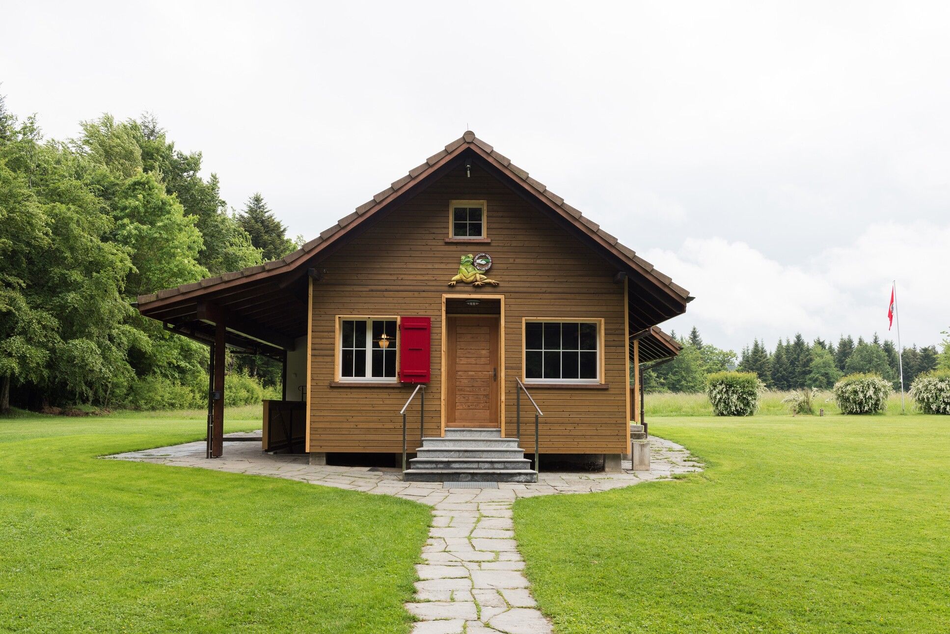 ein kleines Holzhaus mit einer roten Tür und einem grünen Rasen 