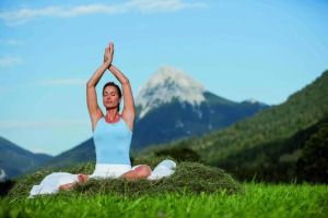 Frau mit einem blauen Top bei ihrer Yogaübung und um Hintergrund befindet sich eine Bergspitze