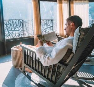 Young man in a robe chilling on a open terrace in the SPA with an amazing mountains view during winter time. Ski resort.